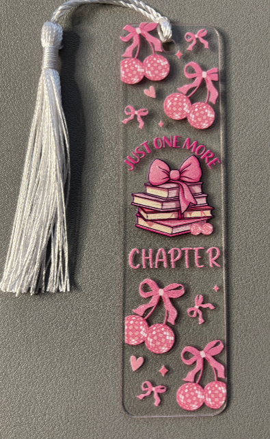 Decorative bookmark with pink designs and tassel and text saying just one more chapter on a gray background