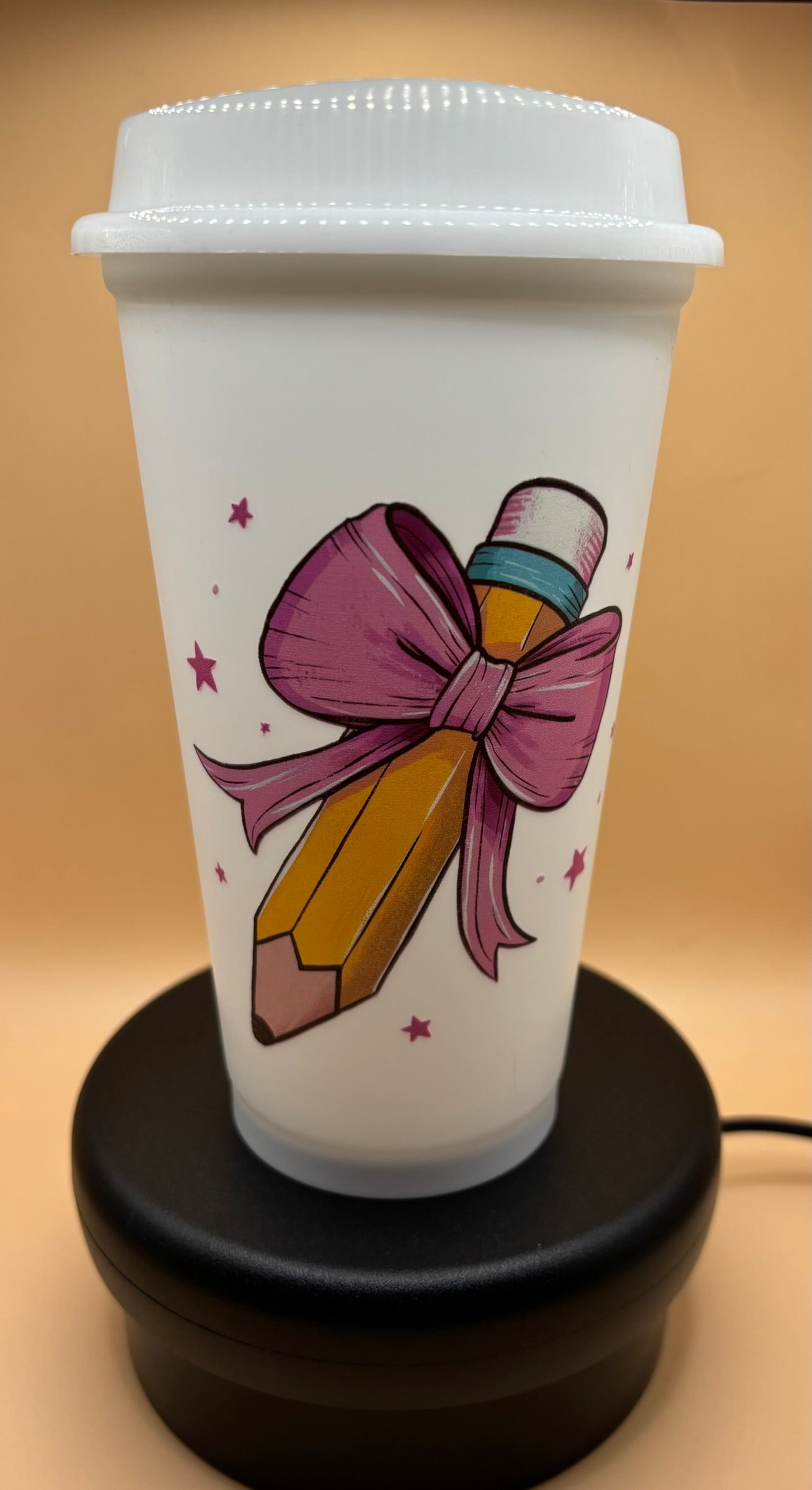 White tumbler with a pencil and bow design on a beige background