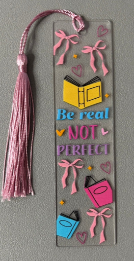 Decorative bookmark with a colorful tassel and motivational quote saying Be real not perfect on a gray background
