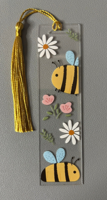 Decorative bookmark with bee and flower designs on a gray background