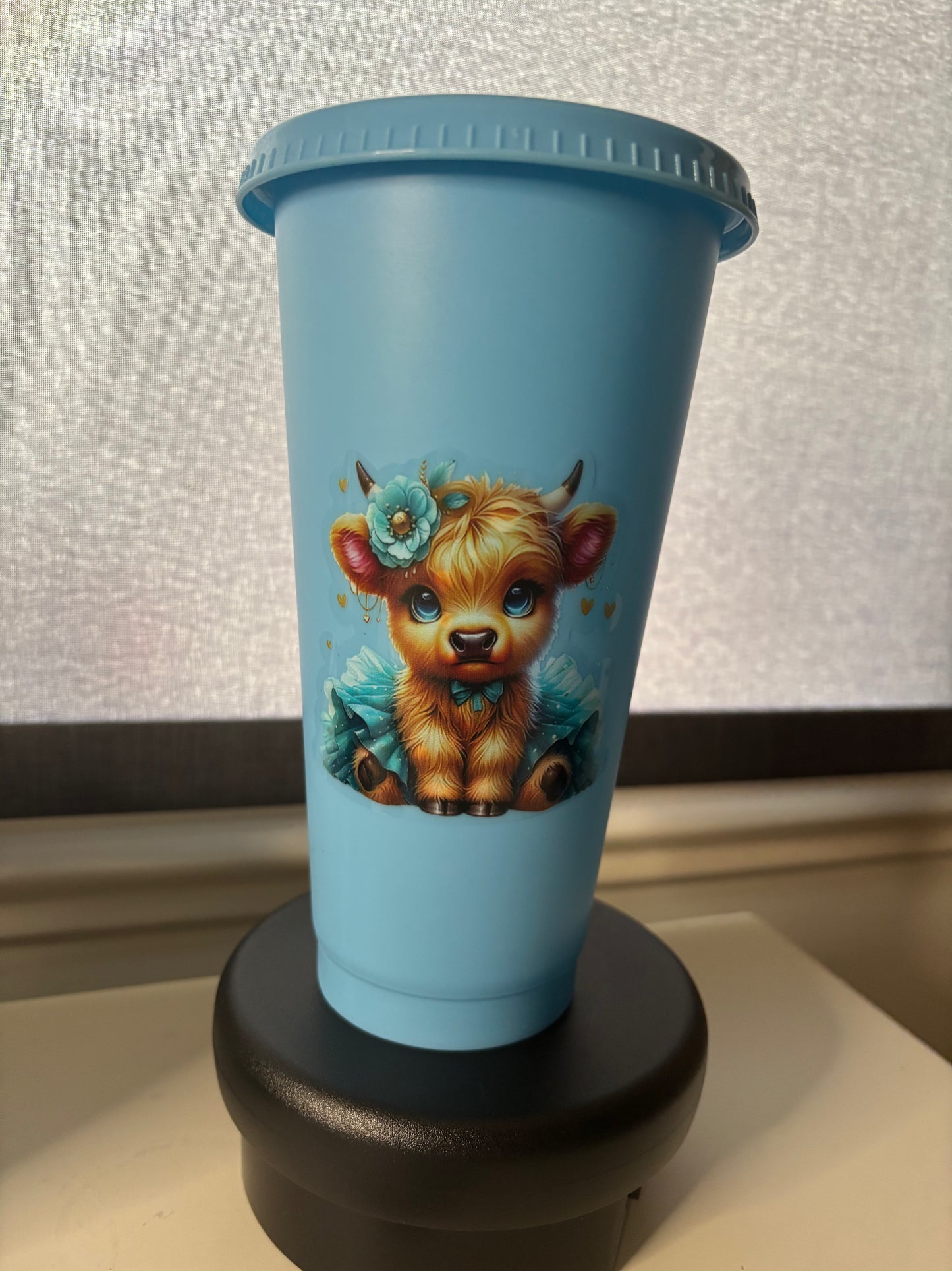 A 24oz blue cold cup tumbler with a Highland Cow decal, a straw lid, and a matching straw.