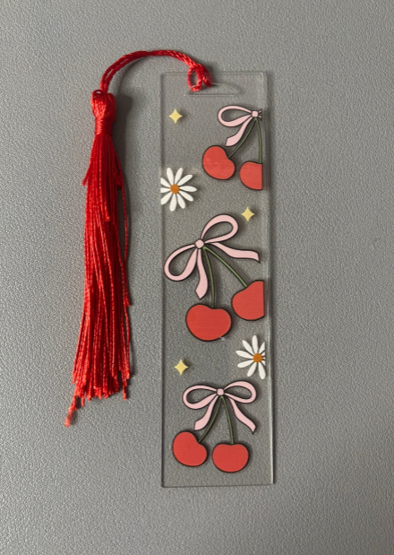 Decorative bookmark with cherries, bows, and a red tassel on a gray background