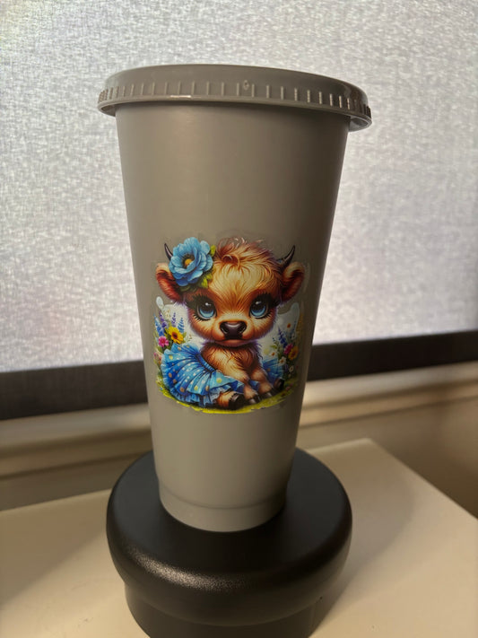 A 24oz grey cold cup tumbler with a Highland Cow decal, a straw lid, and a matching grey straw.