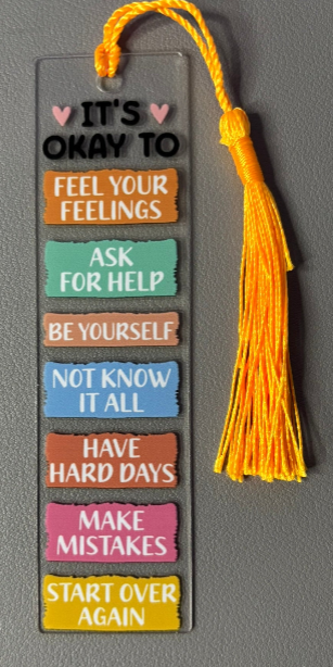 Motivational bookmark with colorful text  stating its okay to be yourself for example on a gray background