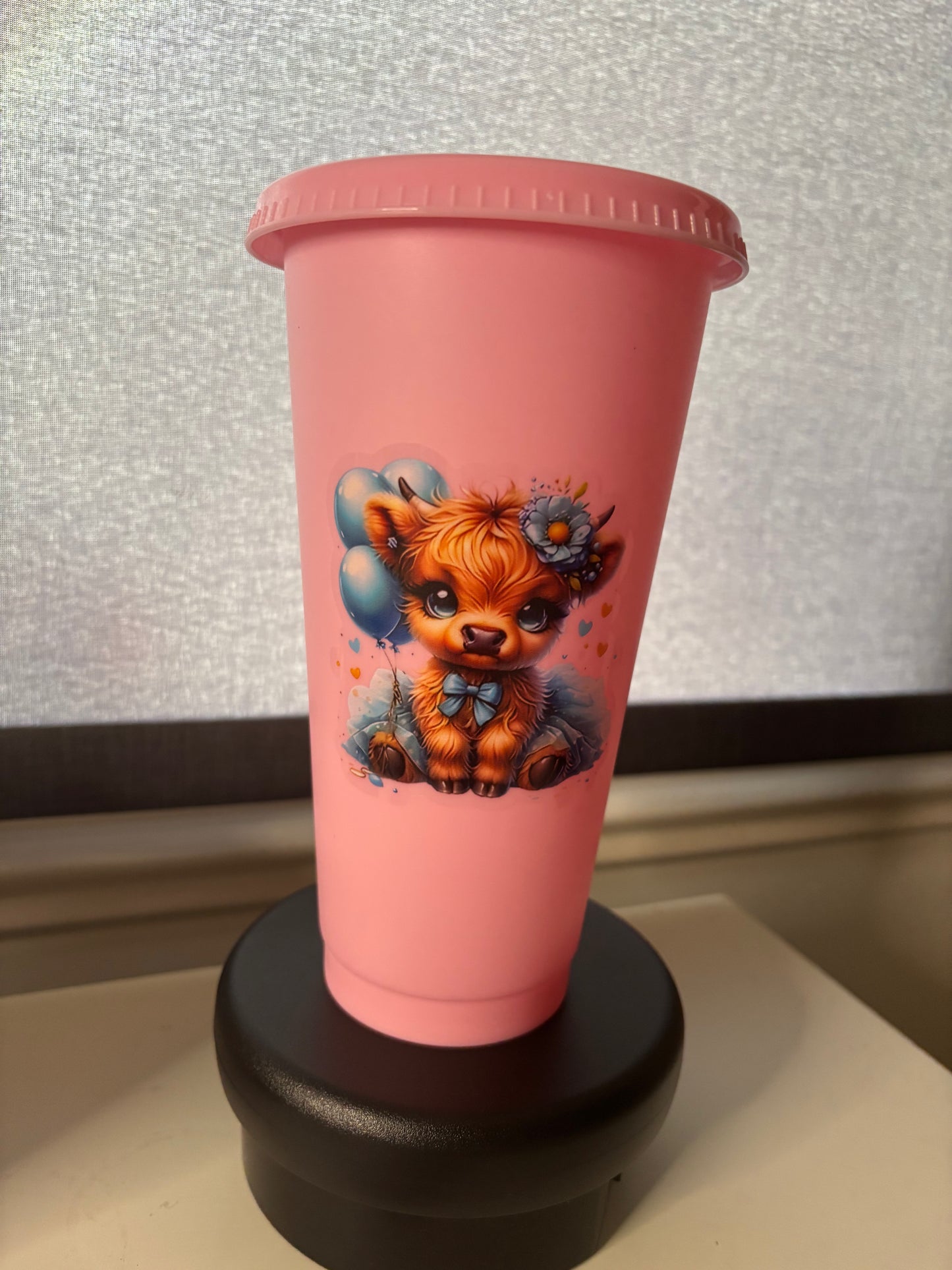 A 24oz pink cold cup tumbler with a Highland Cow decal, a straw lid, and a matching straw.